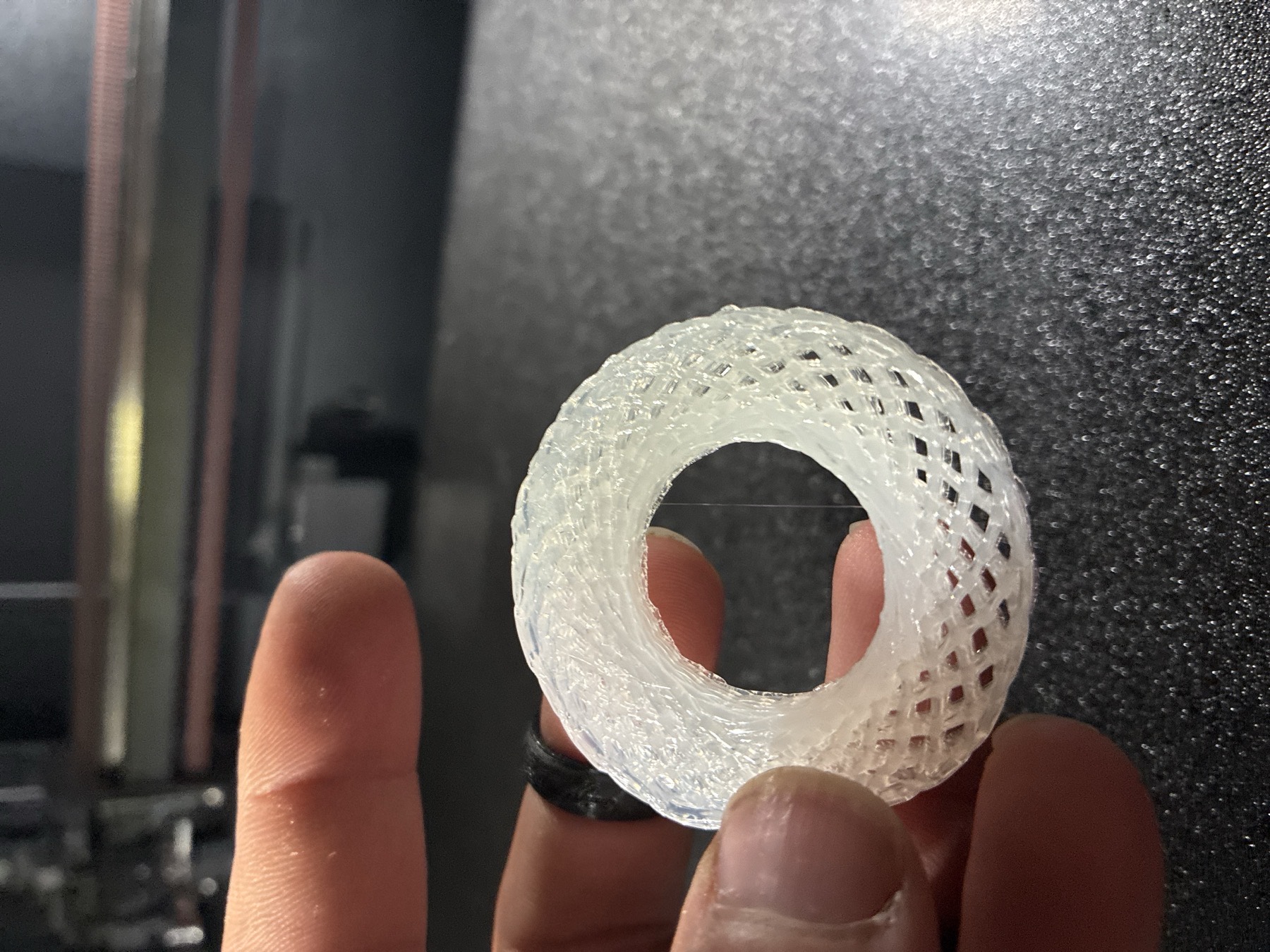 A translucent woven ring, printed as one stroke per layer, held between two fingers